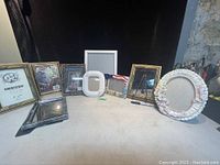 Multiple assorted picture frames displayed on a flat surface with variety of sizes and shapes visible, including a ceramic floral oval frame and ornate gold-tone rectangular frame.
