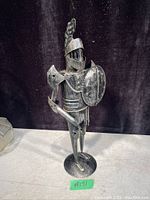 Front view of vintage metal knight figurine in armor holding shield and sword.