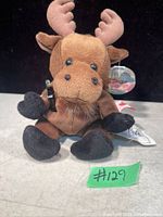 Front view of a brown stuffed moose plush holding a miniature Coca-Cola bottle, with tags attached.