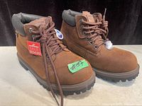 Pair of brown Skechers waterproof boots with tags and sale sticker, size 8.5, lace-up style with padded collar and rugged sole.