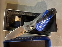 Benchmade Mini-Barrage folding knife opened and resting on box with tag attached.
