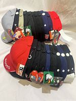 Photo showing two rows of baseball style caps stacked, various colors and with tags attached.