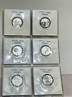 6 steel war pennies individually encased in white coin holders, labeled 'STEEL WAR PENNY'. Coins show profile of Abraham Lincoln and varying wear.