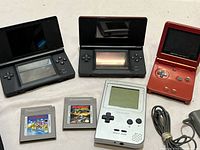 Two black Nintendo DS consoles open and one orange Game Boy Advance SP open with buttons visible