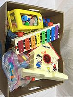 Top view of box showing the vintage Fisher-Price Pull-A-Tune xylophone, yellow peg toy, Snoopy character toy, and bag with plastic parts.