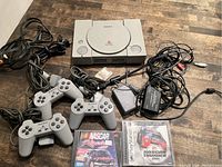 Sony PlayStation 1 console with two wired controllers, power adapter, AV cables, memory card, and two NASCAR games