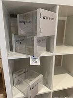 Three IKEA Björnarp clear acrylic display boxes shown in shelving unit, two stacked and one placed beside them.