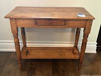 Front view of aged wooden side table showing central drawer and lower shelf with sturdy turned legs.