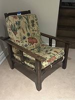 Front, angled view of antique wooden Morris chair with floral cushions showing wood frame and upholstery