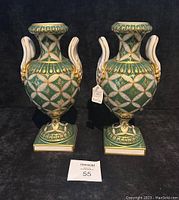 Pair of green and gold antique porcelain vases with white swan handles displayed upright on black background.