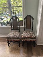 Two barley twist chairs side-by-side by a window showing cane backs and floral upholstered seats with fringe trim.