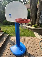 Front view of Little Tikes children's basketball hoop showing the white backboard, red hoop, white net and blue pole with filled base for stability outdoors.