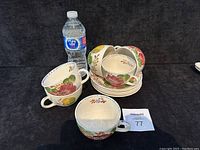 Six Belle Fiore tea cups stacked in the middle with saucers underneath and a single tea cup and saucer in front next to a water bottle for scale.