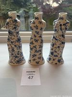 Front view of three porcelain vases shaped like Chinese qipao dresses, showing intricate blue floral designs on white background.