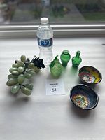 Full overview of the lot including two colorful ceramic bowls, three green glass decorative items, and decorative grapes next to a water bottle for scale.