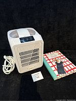 White Wolfgang Puck ice cream maker with power cord and Pidapipo recipe book on a black surface.