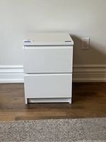 Front view of the IKEA Malm white two drawer nightstand, showing flat drawer fronts and compact design.