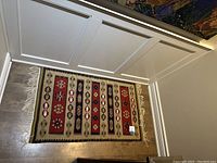 Rug laid flat on wooden floor showing its geometric pattern and fringed edges.