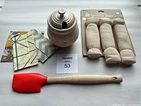 Le Creuset jar, silicone spatula, fabric wax covers, and produce bags arranged on white background.