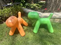 Two dog-shaped Puppy stools (one orange, one green) on grass front view