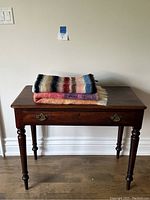 Two folded mohair blankets stacked on a wooden table, showing overall colors and fringe ends.