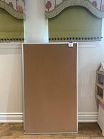 Full view of rectangular cork bulletin board with aluminum frame against a wall.