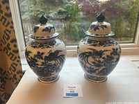 Front view of two blue and white porcelain ginger jars with lids, showing horse and floral designs.
