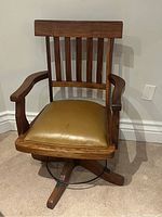 Front view of the vintage bankers chair showing slatted wooden backrest, armrests, and vinyl seat cushion.