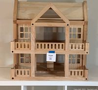 Front view of the three-level wooden dollhouse showing the balconies and window cutouts.