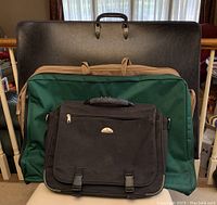 Full view of four bags stacked, including the large black portfolio, green Canine Camper carrier, black Samsonite laptop bag, and brown Pierre Cardin suit bag.