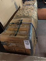 Barcana branded cardboard box containing 8 foot faux Christmas tree secured with blue bungee cords.