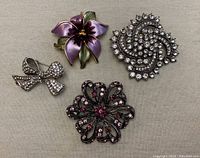 All 4 costume jewellery brooches arranged on beige fabric showing size and details.