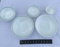 Corelle dishes including salad bowls and plates of varied sizes with green rim pattern, all placed next to a measuring ruler to show scale.