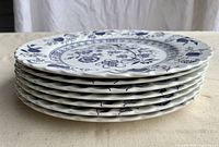 Stack of 7 Johnson Brothers Nordic dinner plates showing the scalloped edges and blue decoration from side view.