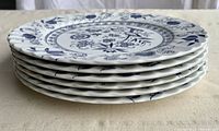 Stack of six white ceramic plates with blue Nordic floral pattern and scalloped edges, showing pattern details and overall condition.