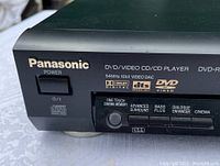Close-up of the front left corner of the Panasonic DVD player showing brand name, power button, and several feature logos including Dolby Digital, dts, and DVD Video.