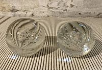 Two spherical clear glass paperweights placed upright, showing internal bubbles and swirl patterns.