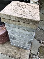 Stacked view of sixteen square paving stones with visible dirt, some surface wear and minor chipping.