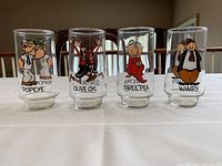 Set of 4 Popeye Coca Cola themed glass tumblers lined up showing full character prints and names