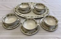 Set of five bouillon cups on their saucers arranged with oval platter at the back, all featuring the green floral pattern on white china