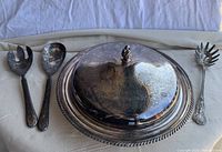 Photo showing the silverplated serving platter with lid, and three tarnished silverplated servers (pasta server, salad fork, slotted spoon) on fabric background.