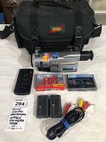 Sony DCR-TRV103 Handycam and accessories including Optrex camera bag, remote, cassettes, batteries, and AV cable laid out for view.