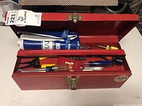 Photo showing open red toolbox with various hand tools including screwdrivers, pliers, and a wrapped item.