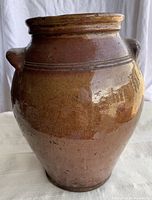 Front view of brown glazed earthenware crock showing overall shape and incised shoulder lines.