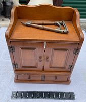Front view of wooden spice chest cabinet with two paneled doors, two knobs, two small drawers, showing wood finish and curved top edge with a measuring scale below indicating size.