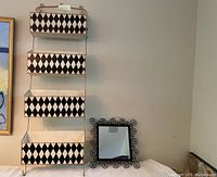 Frontal view of the 4 tier metal storage unit and small decorative mirror, showing the patterned tiers and mirror frame