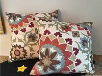 Two geo-floral patterned throw pillows, showing both in an angled position against a wall.