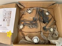 Overview of the wrought iron frame with tarnished silverware pieces and 5 votive holders packed in a box, with an instruction sheet.