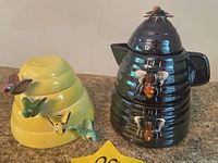 Set of yellow measuring cups stacked with colorful bee-shaped handles and brown honey pot with bee decorations.