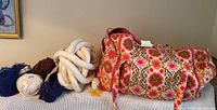 Large quilted floral duffle bag with assorted yarn skeins including thick white cord, blue, brown, and multicolored yarns placed beside the bag.